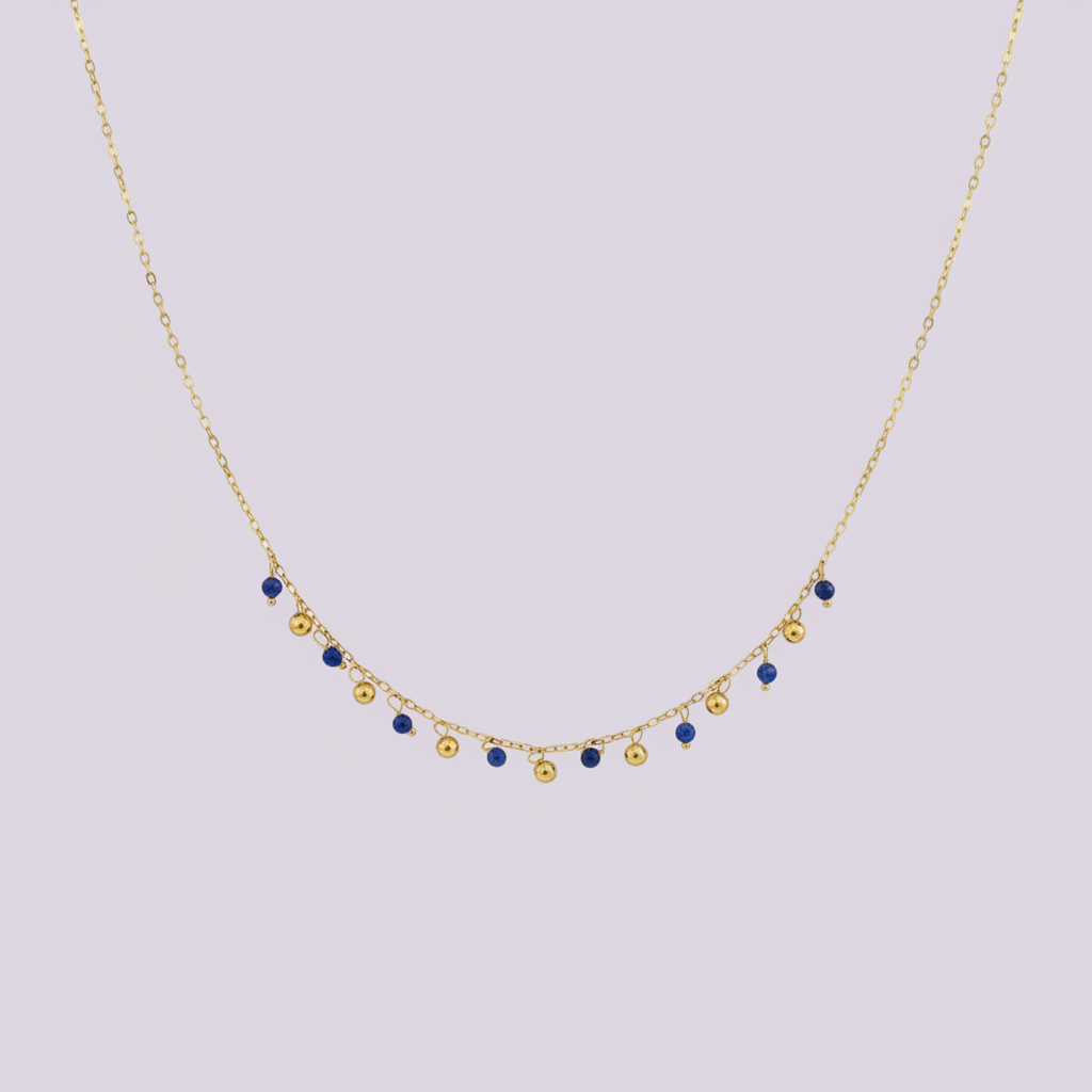 Collier doré avec perles bleues et dorées pendantes sur fond lilas