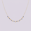 Collier doré avec perles bleues et dorées pendantes sur fond lilas