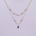 Collier double rang doré avec perles bleues et pendentif médaillon sur fond lilas